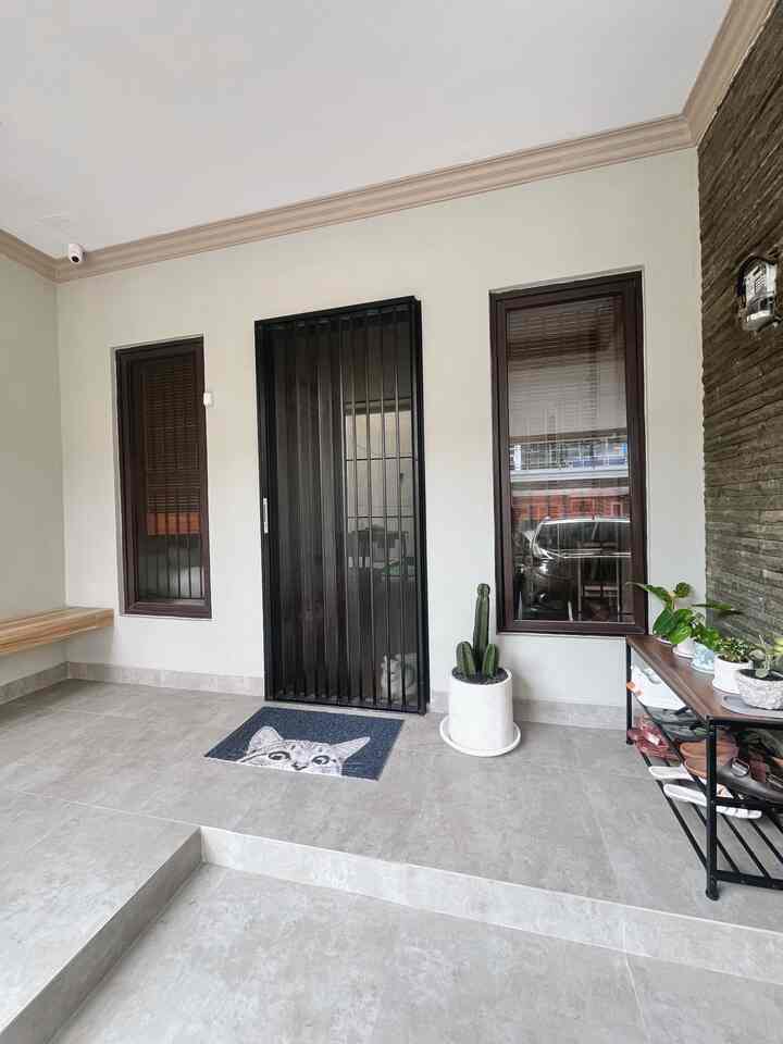 Entrance featuring gray tiled floor and black metal gate door, cat visible behind gate, with bench and plants arranged aesthetically