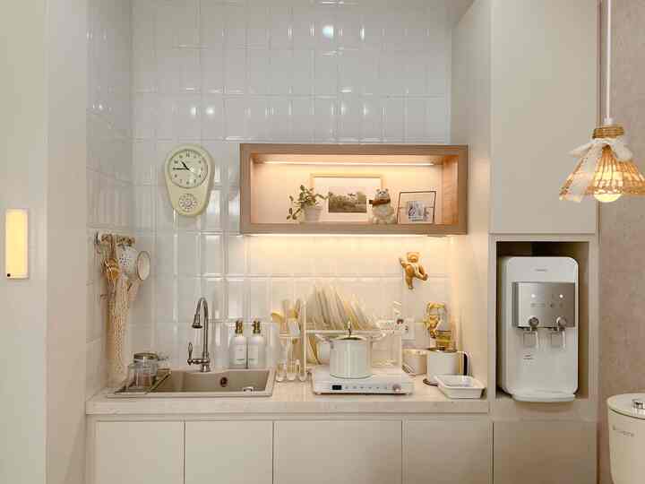 Bright white-toned kitchen featuring a vintage wall clock, open storage shelf with decor, and compact functional layout