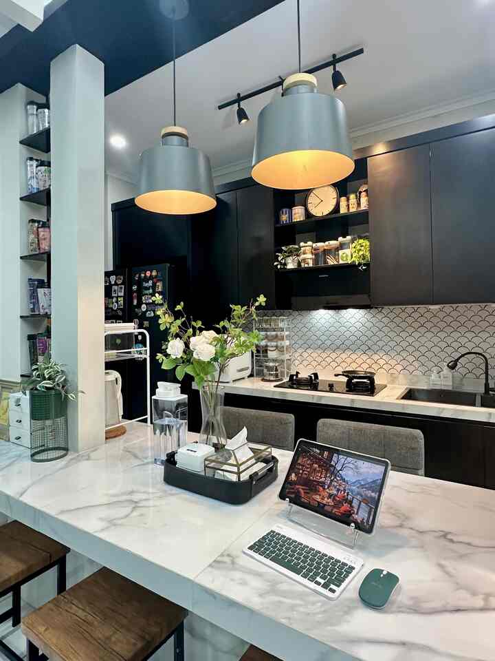 Modern kitchen in black and white tones featuring a marble dining island, pendant lighting, and a home office setup