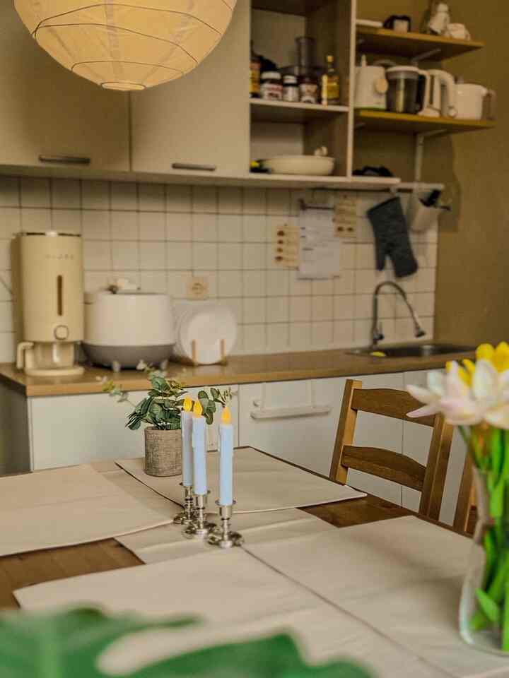 Natural color toned kitchen space featuring a wooden dining table with white taper candles creating a cozy atmosphere