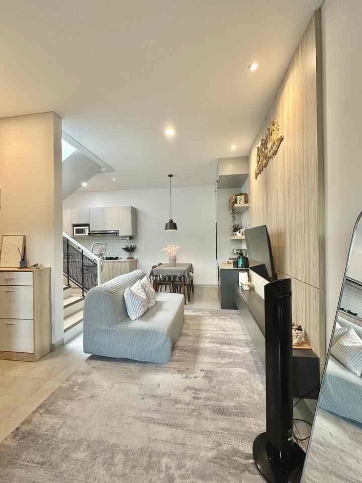 Bright white and gray toned open plan living room and kitchen featuring a simple modern sofa and dining table in a spacious, comfortable setting