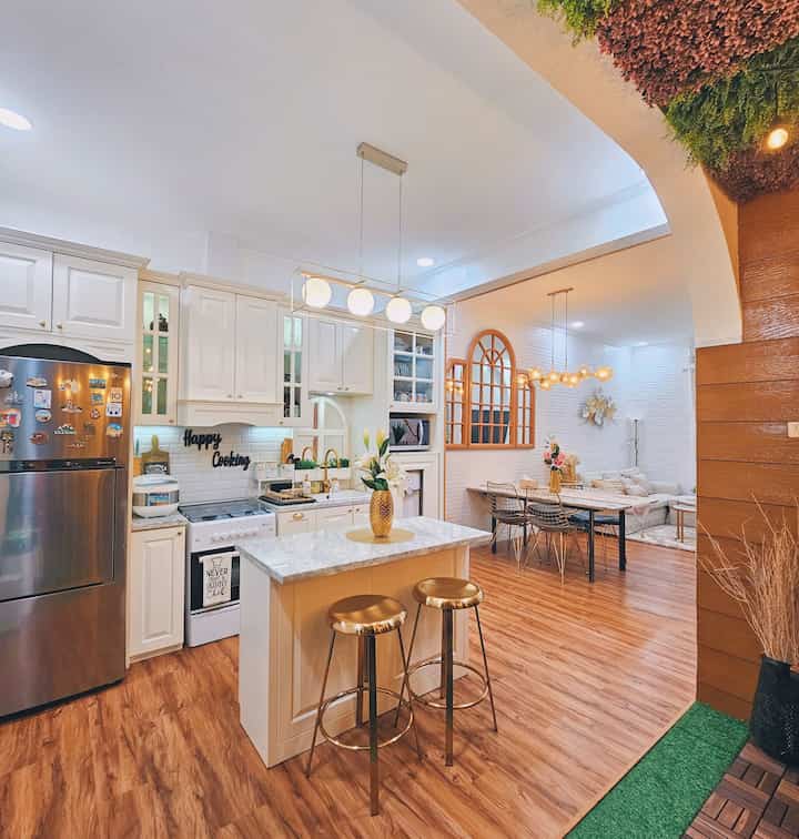 Modern kitchen and dining room featuring bright white and gold accents, warm wood-tone flooring creating an open and cozy atmosphere