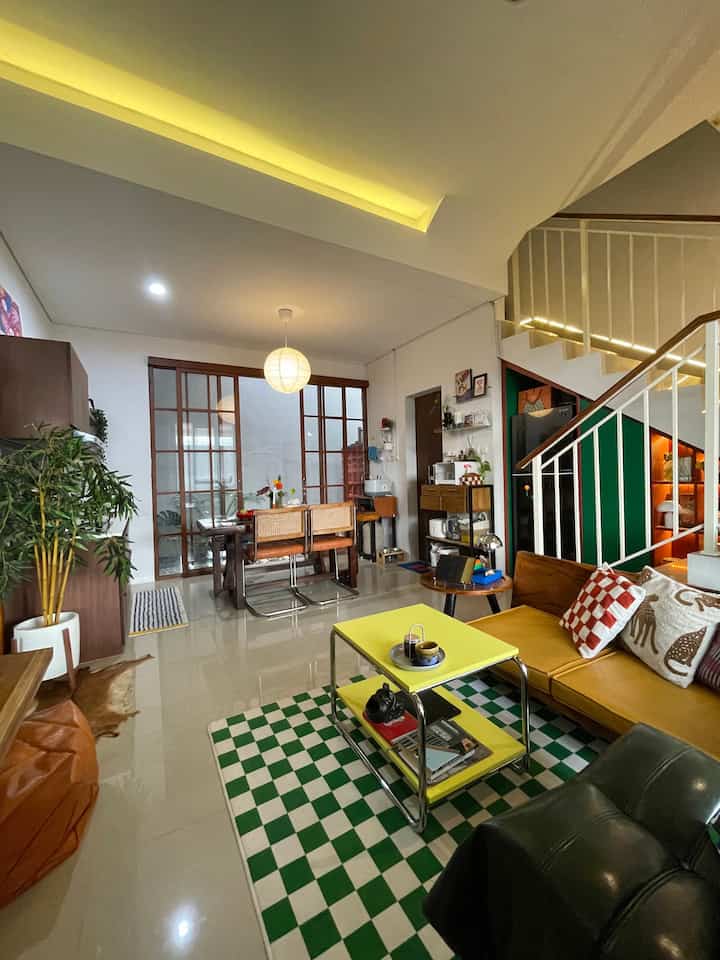 White-walled open space featuring living room and dining area with green checkered rug and yellow coffee table accents