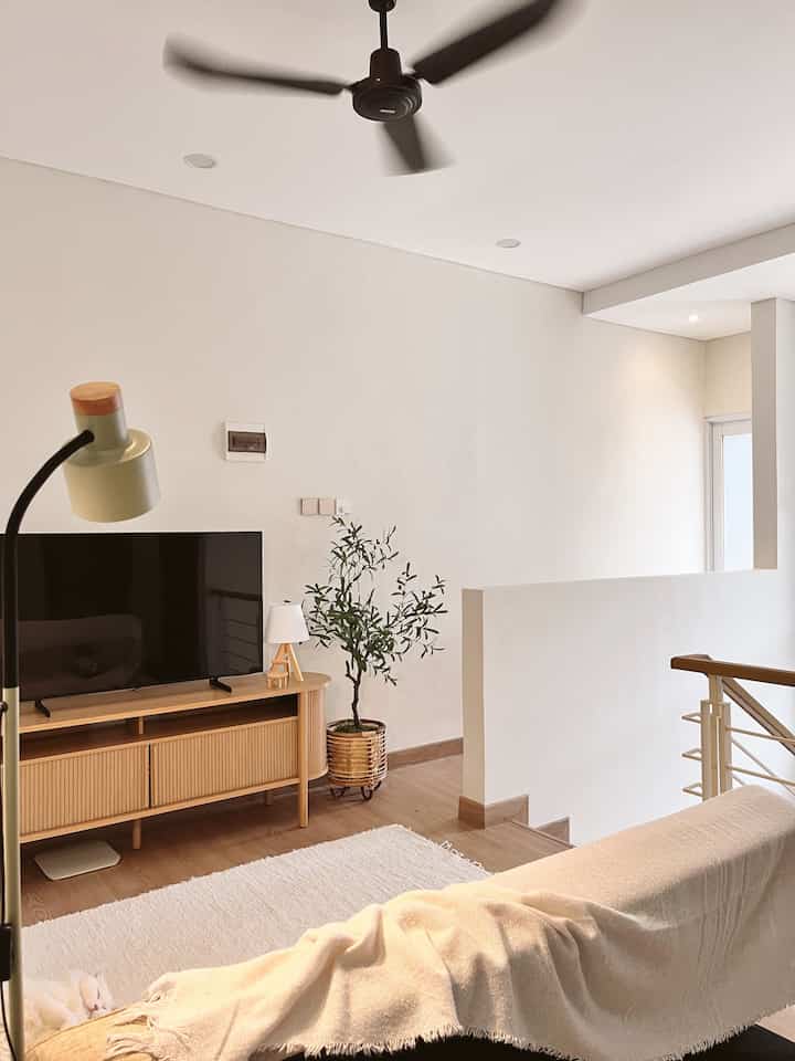 Cozy loft living room in white and wood tones featuring a sofa bed, TV stand, and ceiling fan with a relaxing atmosphere