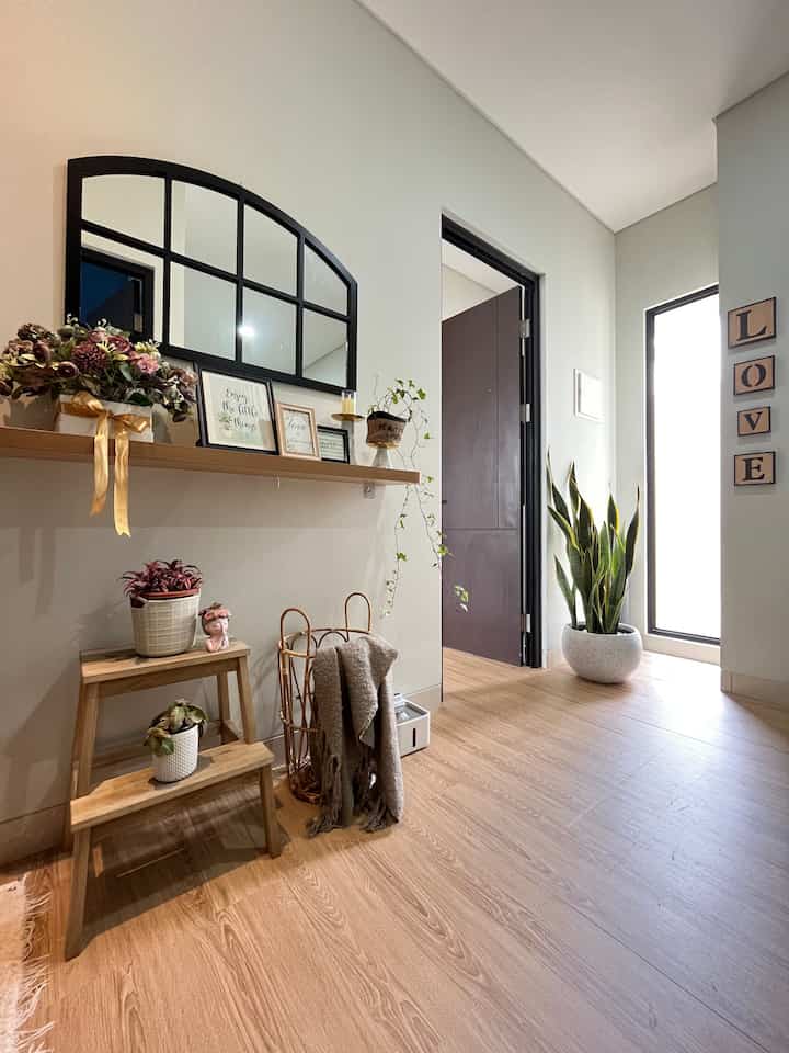 Natural color wood-tone entrance featuring black frame mirror, potted plants, and simple decorative elements with a cozy atmosphere