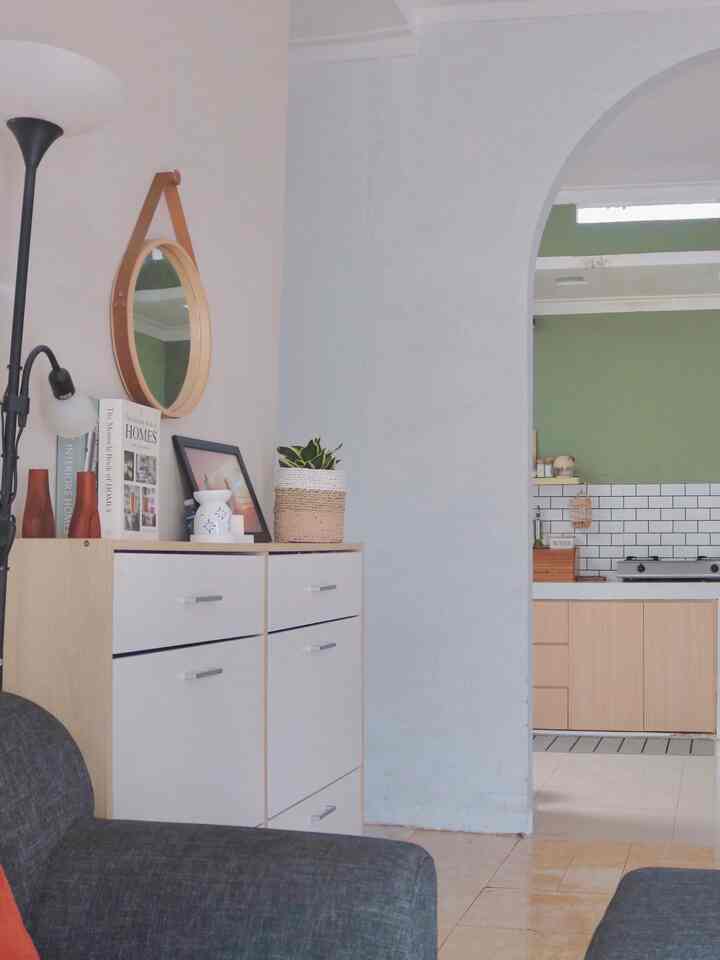 White and natural tone living room featuring dark gray sofa, round mirror, and bookshelf cabinet in a clean setting