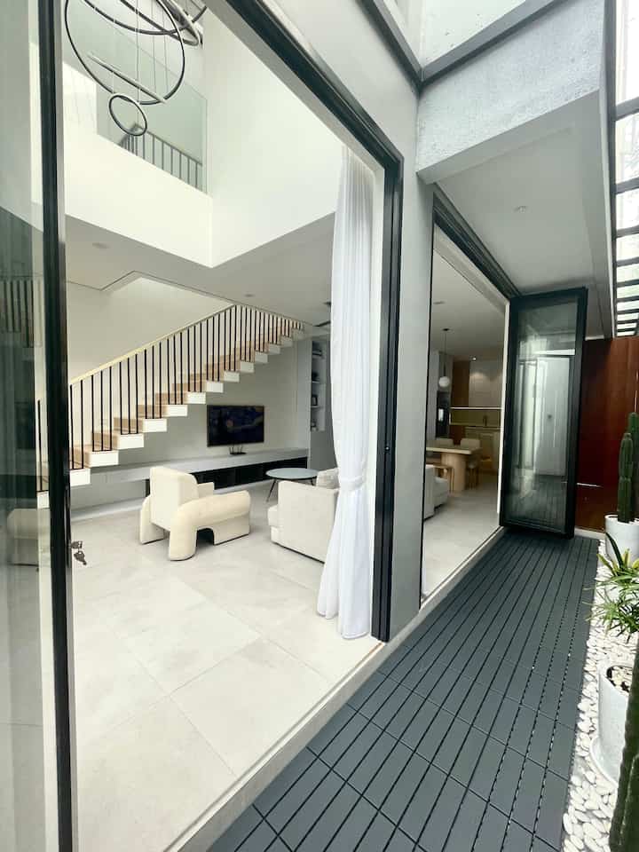 Bright modern living room featuring white sofas, staircase, and large windows providing a spacious atmosphere
