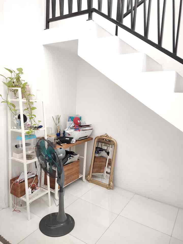 White-toned compact space featuring desk and shelving under stairs, neat corner of living area