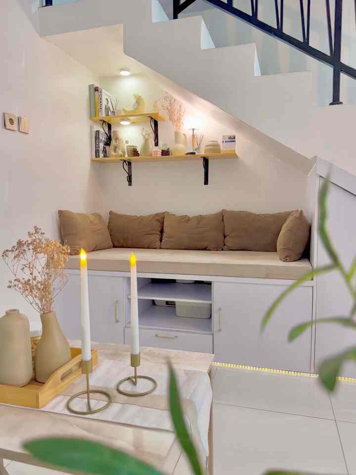 Natural living room under white staircase with beige cushions, cozy relaxation area decorated with tray and candles