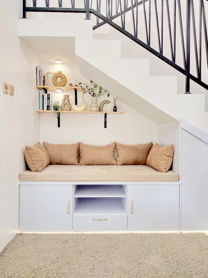White walls and custom cabinet forming a cozy corner with beige cushioned bench underneath stairs