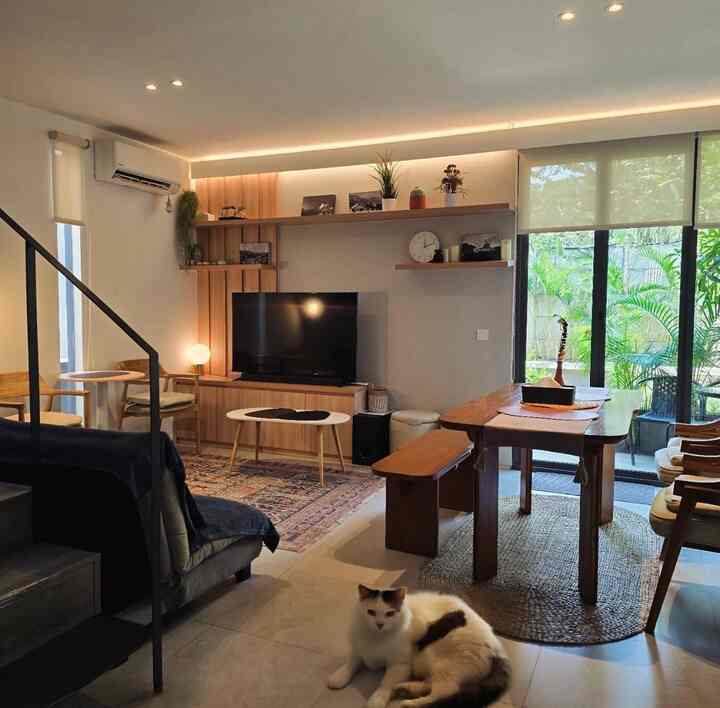 Natural wood tones and white walls define a cozy open living and dining space featuring a cat lounging on the floor