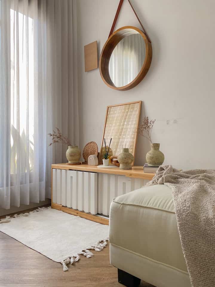 Natural wood tone and white corner living room featuring simple furniture, a round mirror, and a rug with warm cozy atmosphere