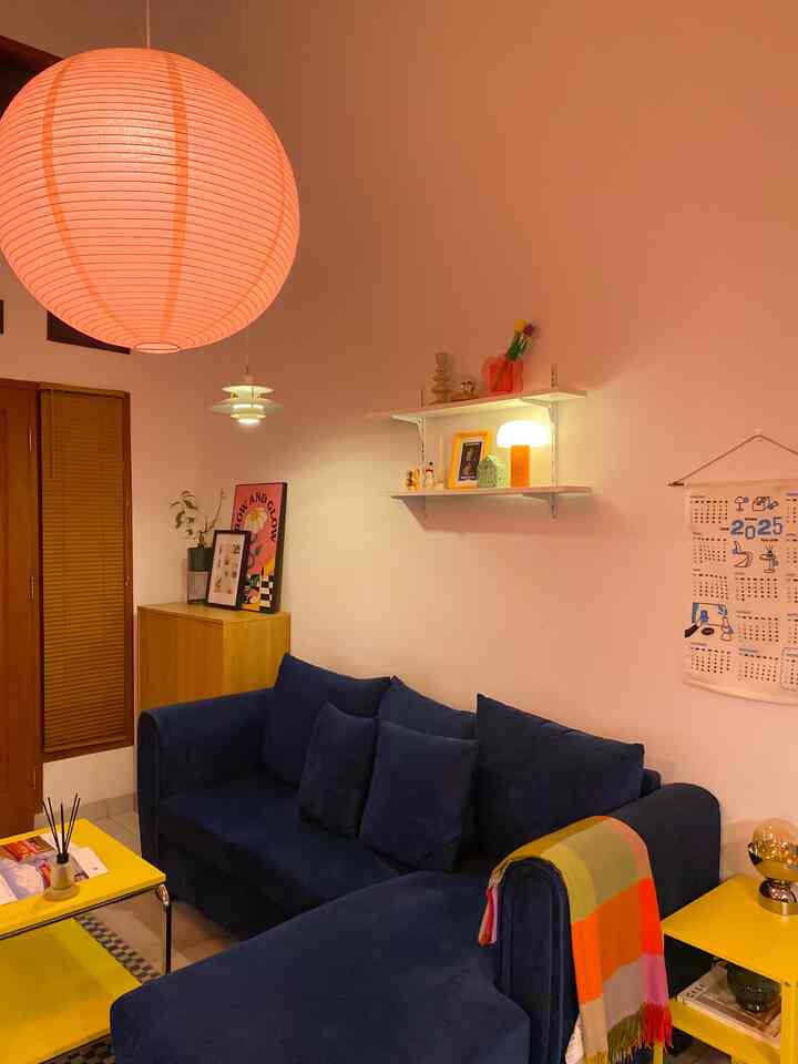 Natural tone living room featuring a blue sectional sofa, bright orange pendant light, and yellow tables creating a warm atmosphere
