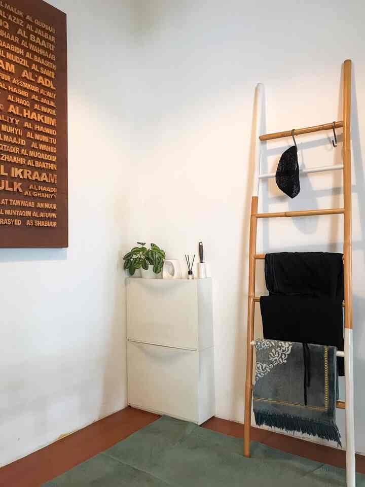White and wood tone small entrance space featuring a shoe cabinet and a leaning ladder used as shelf in a minimal interior