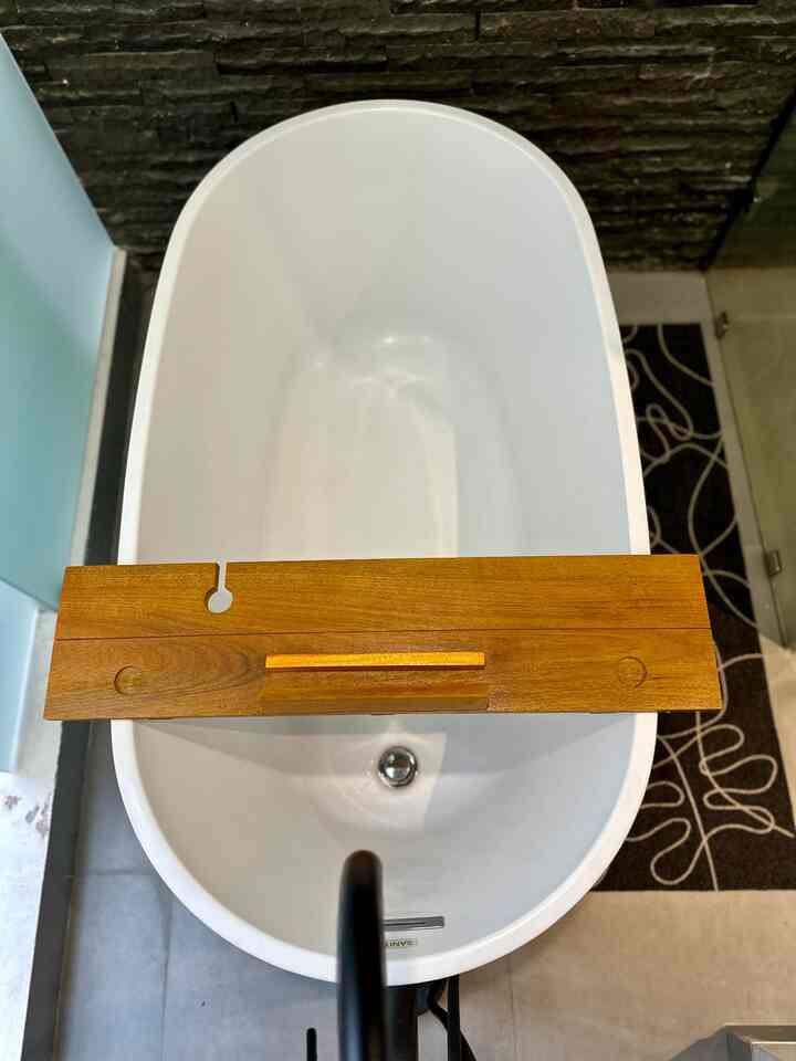 White bathtub featuring a wooden tray with dark stone wall tiles in a bathroom setting