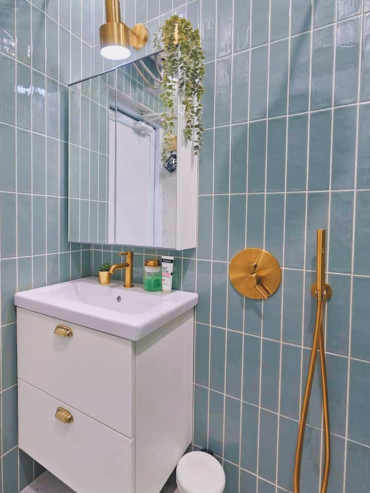 Modern bathroom with green tile walls and gold fixtures, featuring a white sink cabinet and mirror cabinet in a clean setting