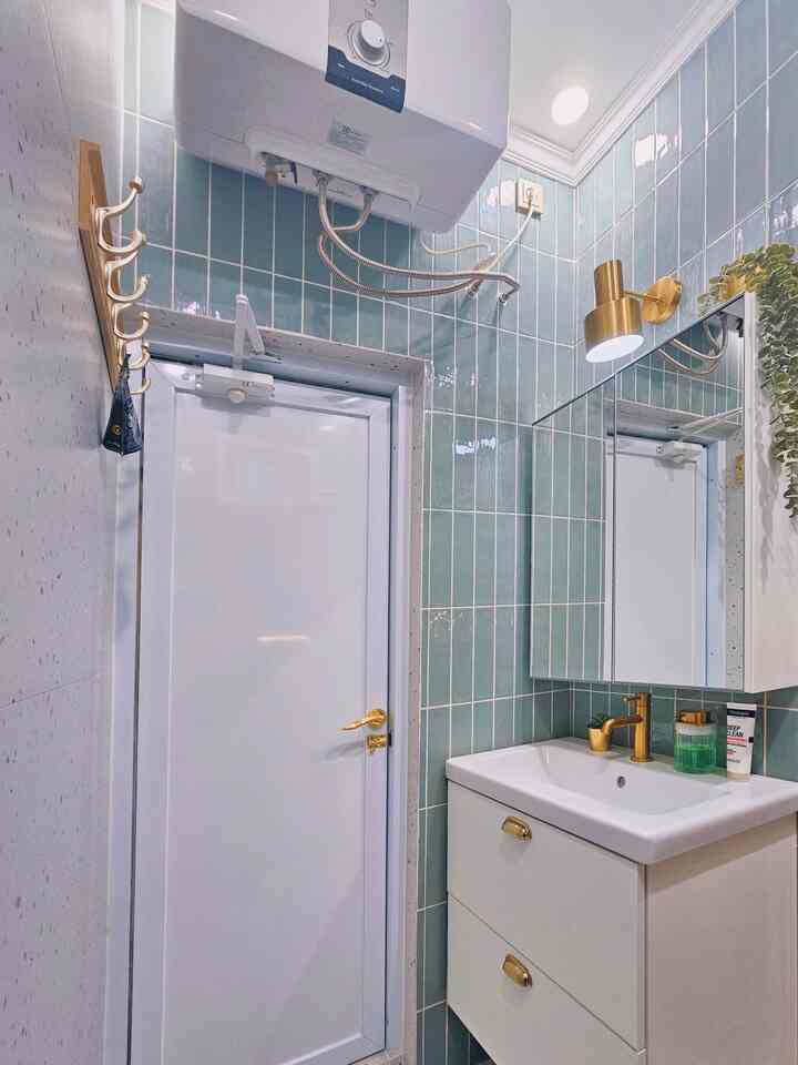 Compact bathroom with white and green tiles featuring gold fixtures and lighting creating a modern elegant atmosphere