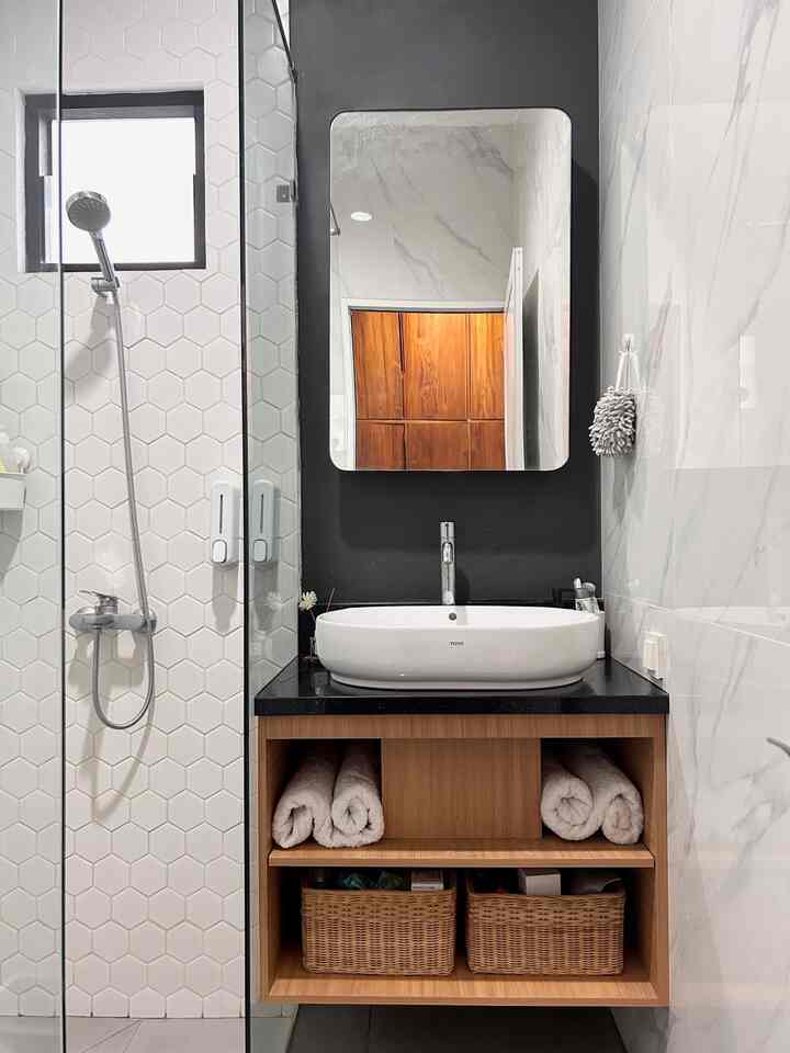 White and wood tone bathroom featuring sink basin, mirror, towels, and wicker baskets neatly arranged in a clean setting