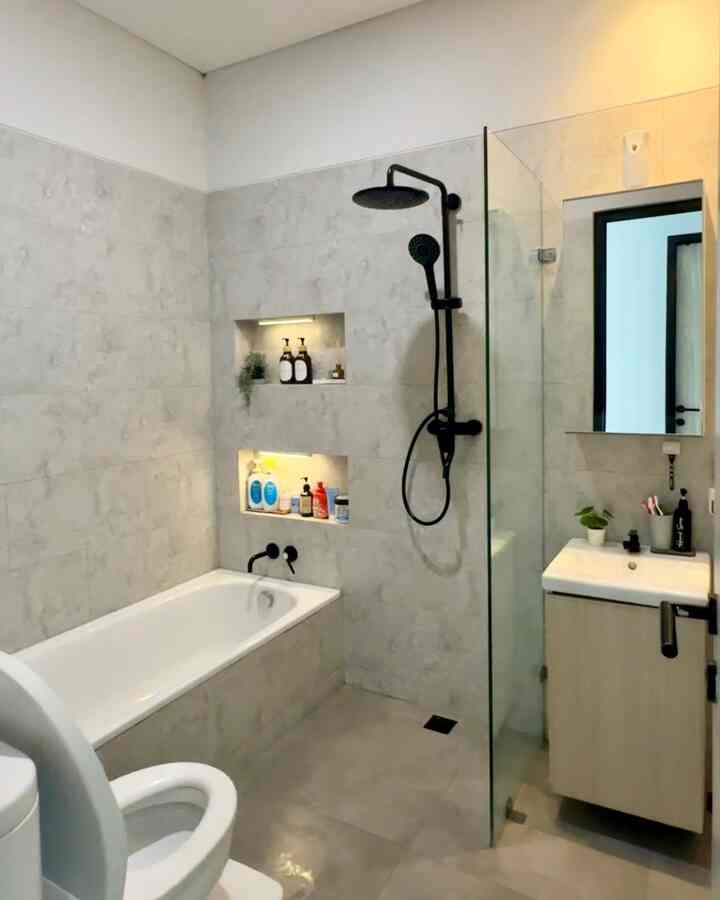 Modern bathroom in gray and white tones featuring a bathtub and black shower fixtures in a clean, compact space