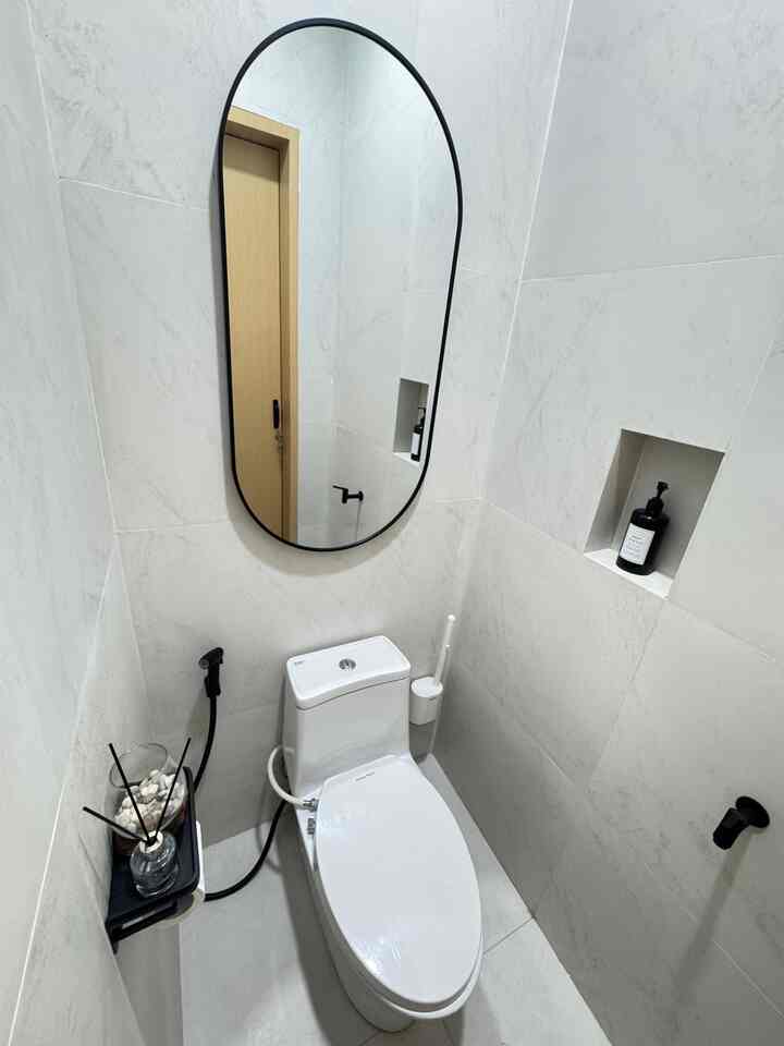 White-toned compact and minimal bathroom featuring a large black-framed mirror and a compact toilet in a neat space
