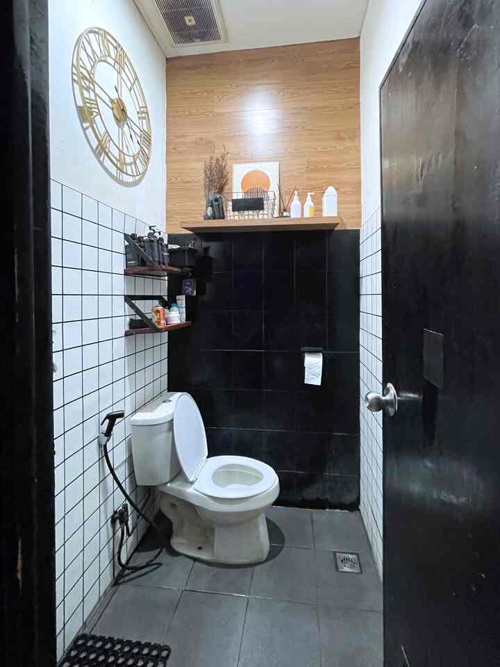 A black and white tiled bathroom featuring a large gold clock and storage shelves, presenting a neat and organized space