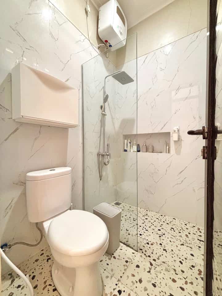 White and beige toned bathroom featuring ceramic toilet and tempered glass shower partition with a clean modern ambiance