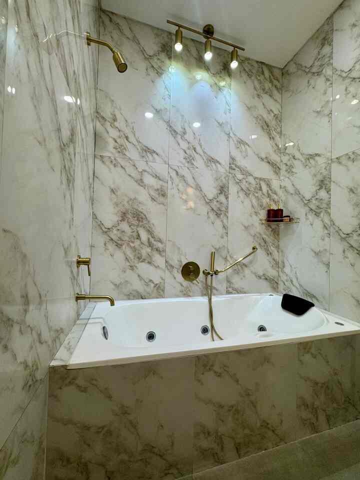 A luxury bathroom featuring white and natural-toned marble tile walls with gold accessories