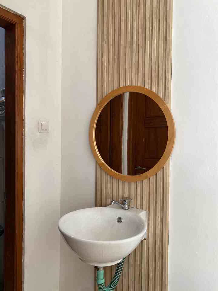 Natural tone wood-framed round mirror and vertical wood wall panel above white wall with a wall-mounted bathroom basin, creating a minimalistic wash area