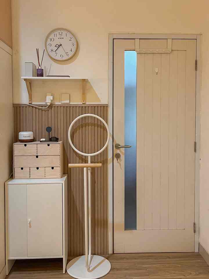A clean entrance space in white and natural tones, featuring a cabinet and wall clock with a cozy atmosphere