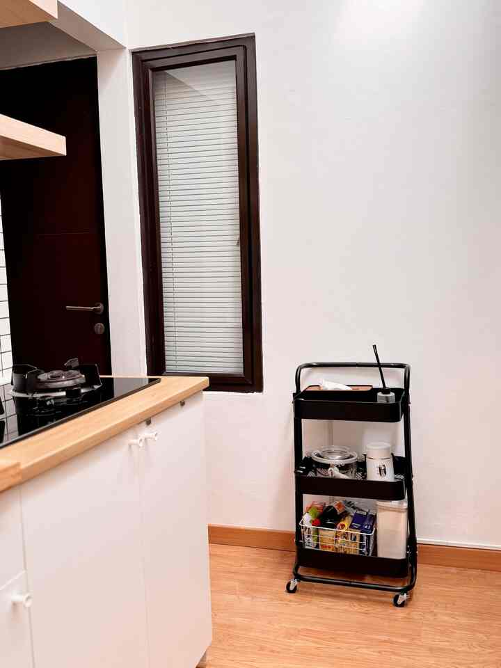 Small kitchen space with white walls and natural wood-toned floor featuring a black kitchen cart