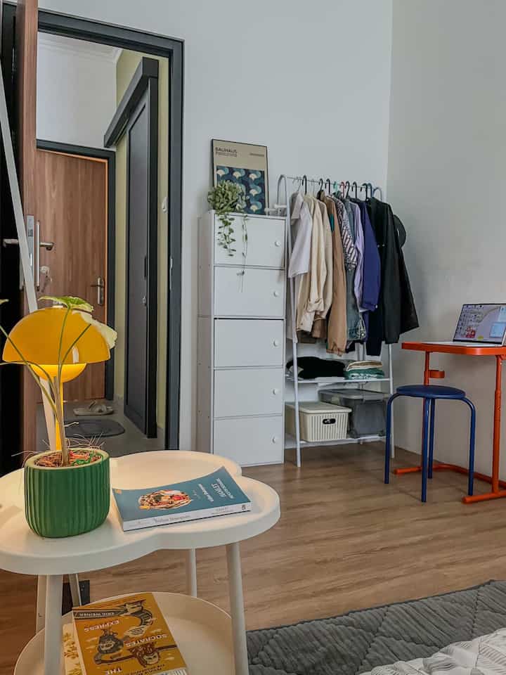 A simple single household room in white and wood tones, featuring an orange desk and stool ideal for remote work