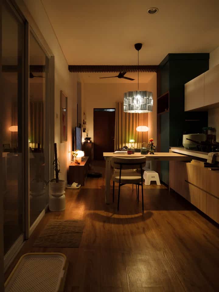 Warm wood-toned floor and yellow lighting in an open kitchen and dining room space