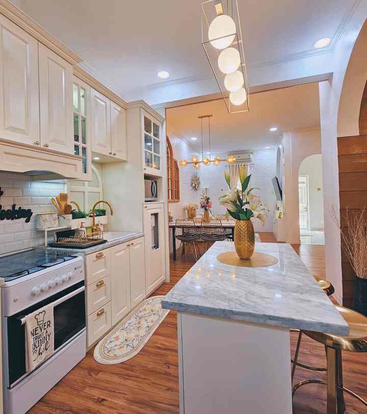 Spacious kitchen and dining room in white and wood tones, featuring gold accent lighting and a kitchen island, creating a cozy ambiance