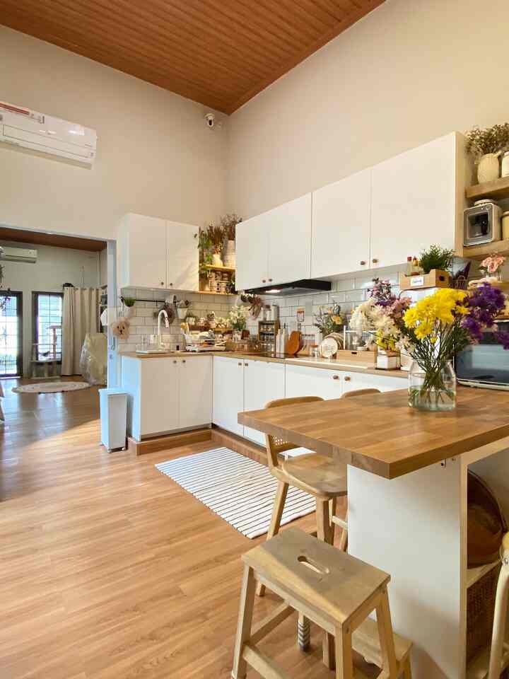Natural-modern kitchen with wood flooring and white cabinets, featuring a wood dining table with a floral vase, creating a warm atmosphere