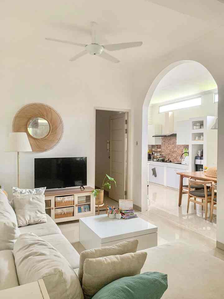 Bright white-toned living room and kitchen space featuring natural wood furniture, sofa, and an arched doorway in a simple and cozy interior