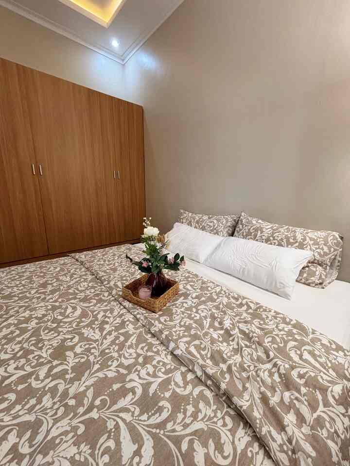 Beige and natural-toned bedroom featuring a large bed with patterned beige duvet and white pillows alongside a wooden wardrobe creating a cozy atmosphere