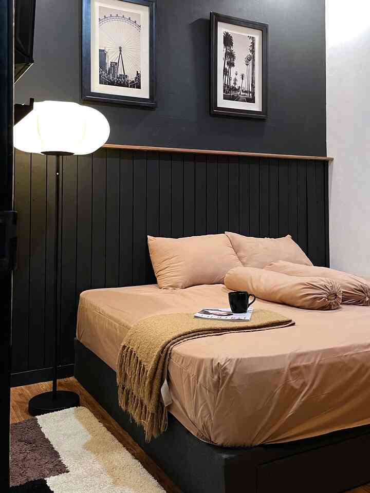 Cozy bedroom with black tone wall and beige bedding, featuring standing lamp and simple framed pictures creating a relaxing atmosphere