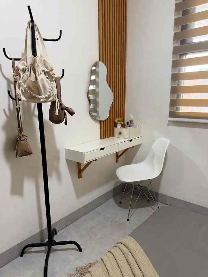 A modern entrance space with white and wood tones featuring a wall-mounted storage cabinet, white chair, and black coat rack creating a clean aesthetic