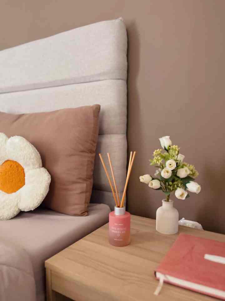 Natural beige and brown tone bedroom featuring pillow and flower vase on wooden nightstand, creating a cozy atmosphere