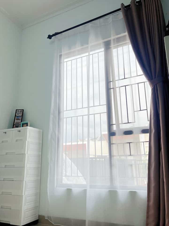 White walls and floor with dark brown blackout curtain on right side and transparent curtain in center at veranda window interior