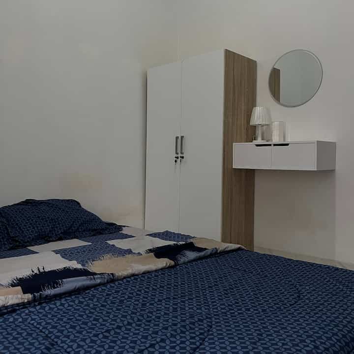 White and navy toned square bedroom featuring wardrobe, round mirror, and minimal furniture for a simple space