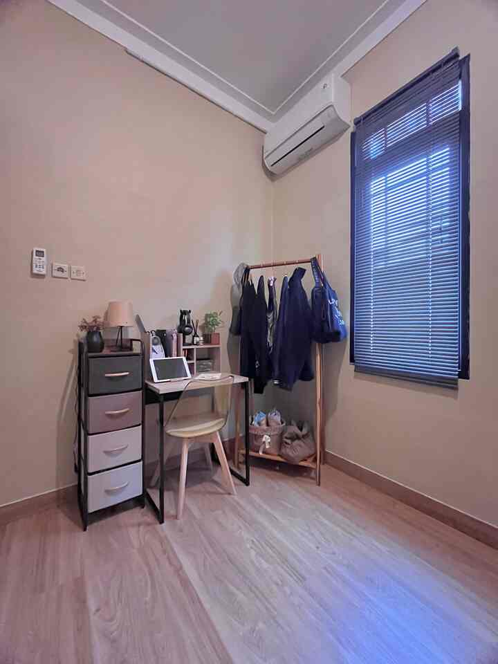 Beige-walled small home office with wood-tone flooring, featuring a desk, office chair, and clothes rack in a cozy setting