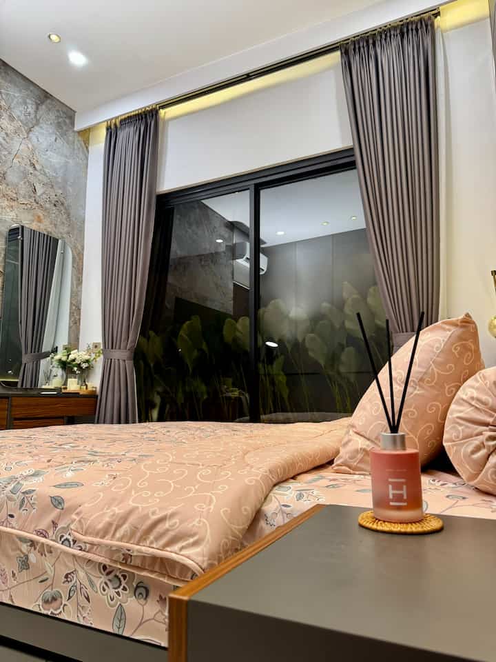 Light brown natural-toned bedroom featuring patterned bedding, curtains, and diffuser in a cozy space