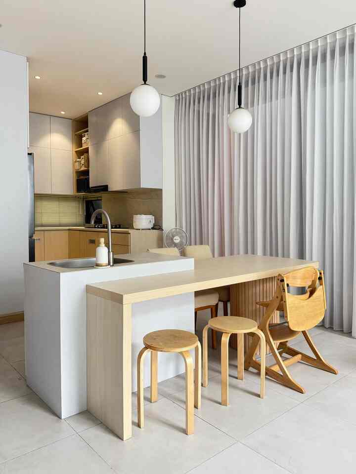 White and beige toned kitchen and dining space featuring natural wood furniture and a baby chair in a modern setting