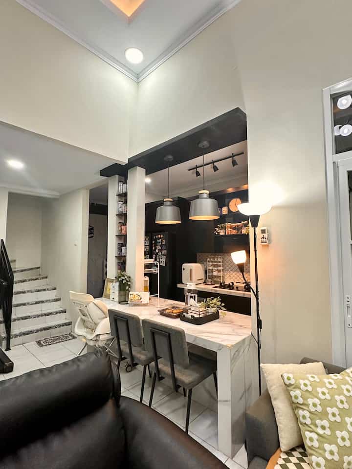 White-toned open kitchen connected to living room, featuring marble dining table and pendant lights in a modern design
