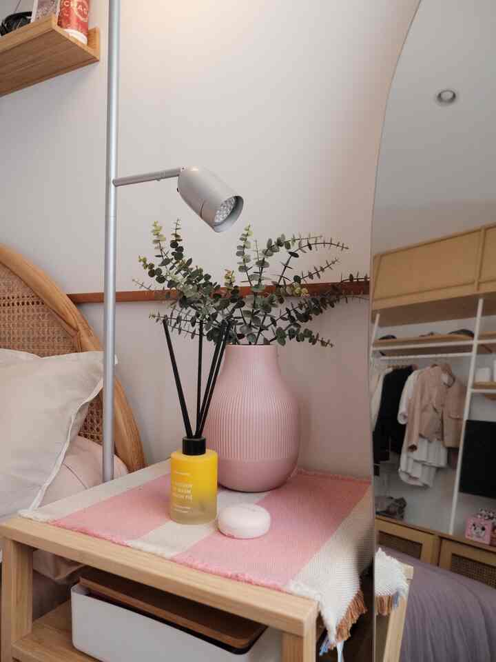 Warm-toned bedroom nightstand featuring a pink vase and table runner on a wood-tone side table
