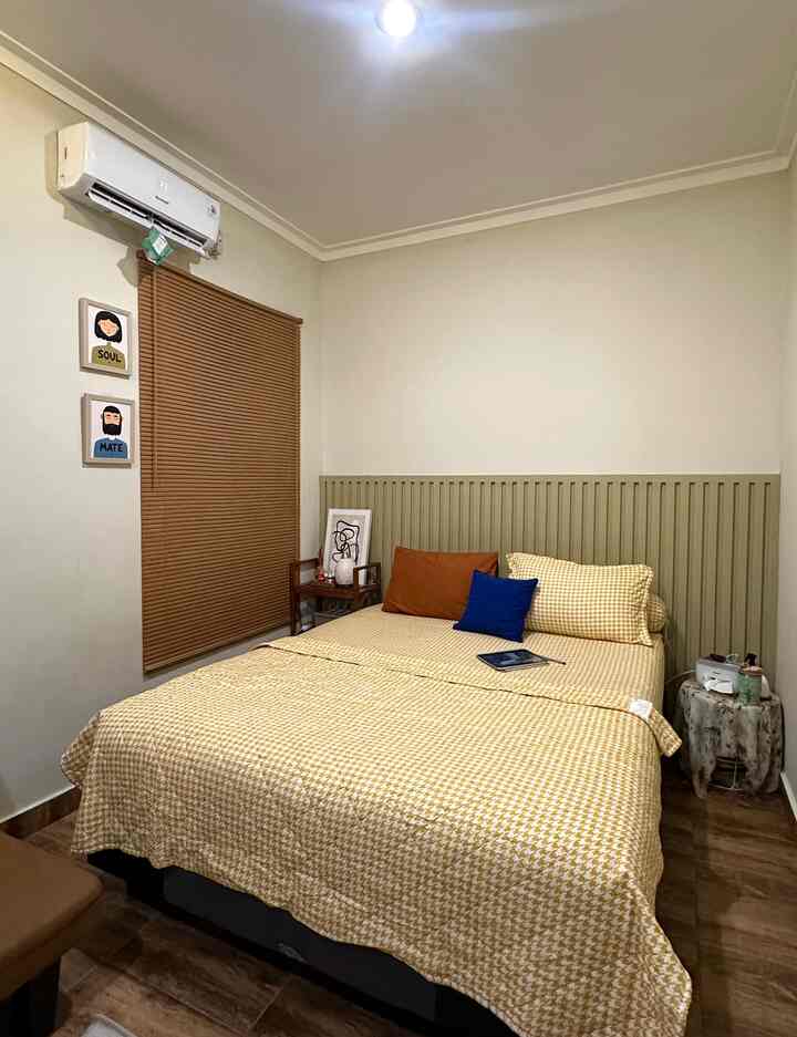 A compact bedroom with warm wood tones and yellow bedding, featuring blinds on the window creating a cozy atmosphere