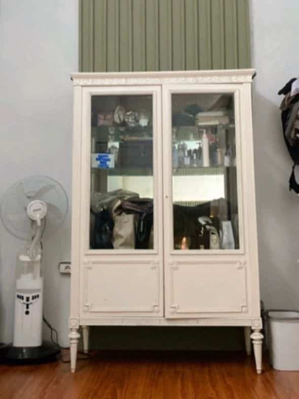 White storage cabinet centered in a small room interior, 16-inch standing fan on the left and wooden floor creating cozy atmosphere