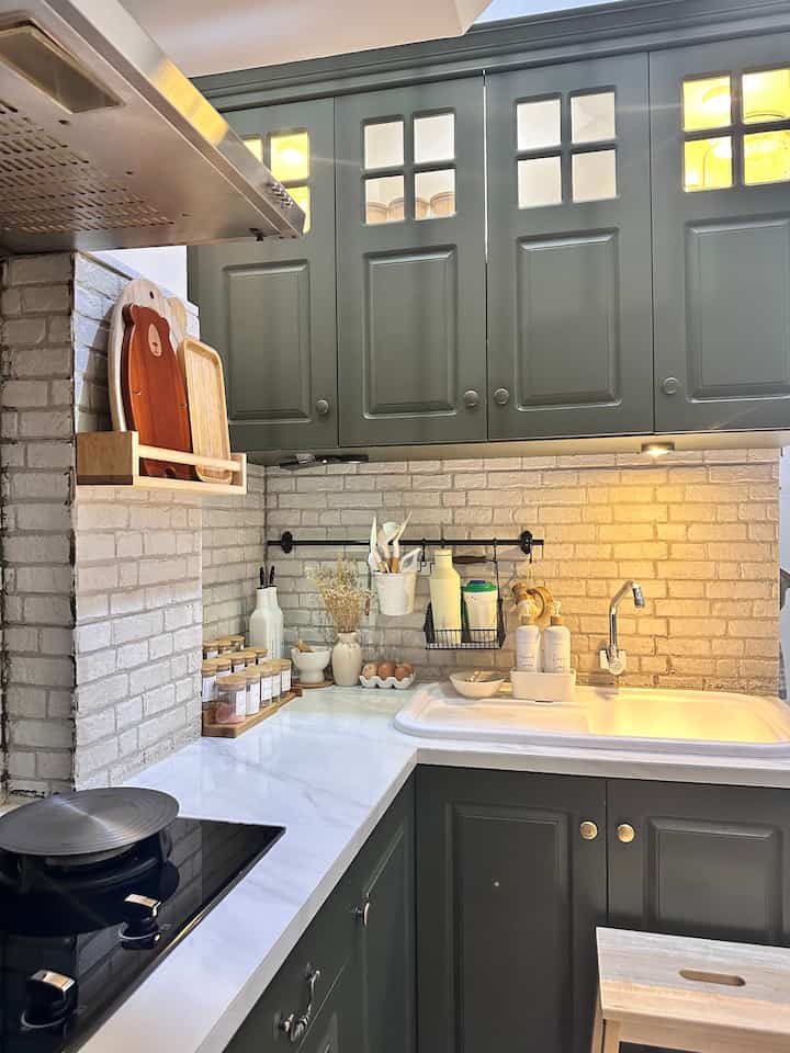Green and white toned compact kitchen with brick-patterned backsplash and storage solutions, featuring retro-style cabinetry and accessories