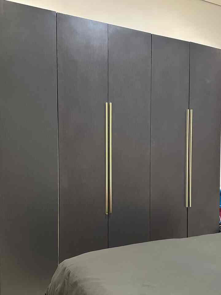 Dark gray built-in closet with golden handles in bedroom space featuring gray bedding
